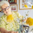 Senior woman arranging flowers in a vase at home.