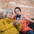 Granddaughter helping grandmother to use the mobile phone at home.