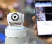 CCTV camera in the foreground and a hand holding a mobile phone in the background