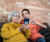 Granddaughter helping grandmother to use the mobile phone at home.