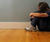 A young boy sits alone in the corner of a room