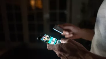 Close-up on a person betting online at home on their cell phone using their credit card.